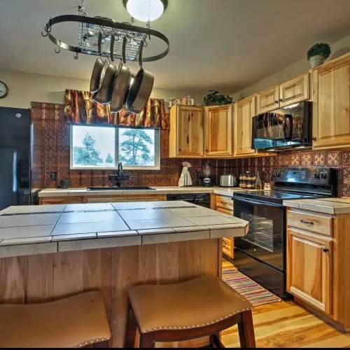 Cozy kitchen with wooden cabinets, a central island, and hanging pots, featuring modern appliances and a warm color scheme.