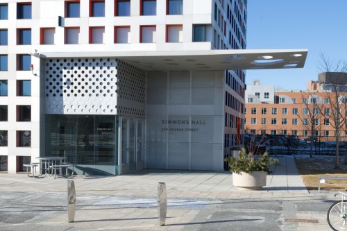Modern building entrance with a sign for Simmons Hall, featuring a unique facade and surrounding pavement.