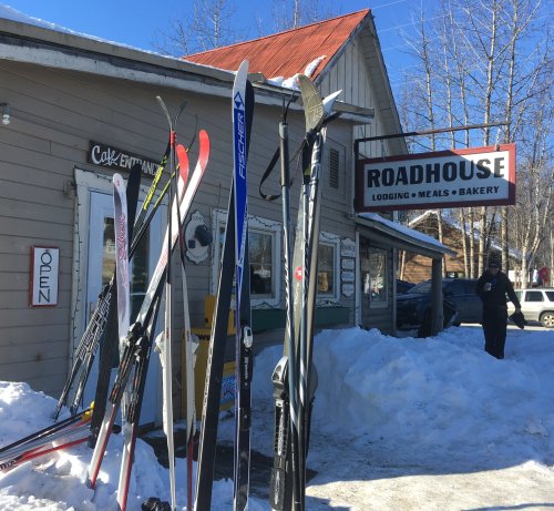 A cozy roadhouse with skis outside, snow on the ground, and a sign indicating it's open for lodging and meals.