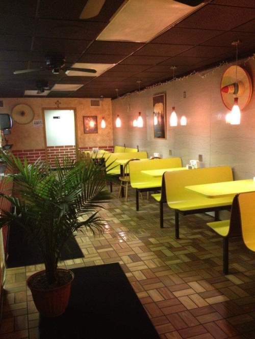 A cozy restaurant interior with yellow tables, a potted plant, and warm lighting, featuring a tiled floor and wall art.
