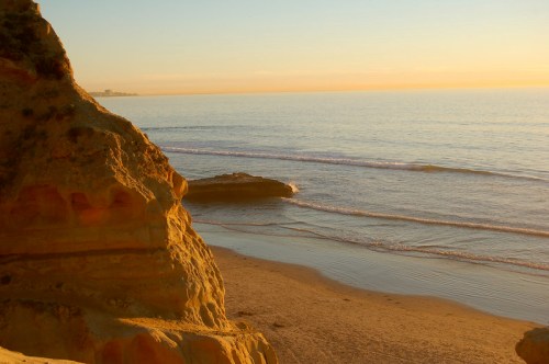Sunset over a calm beach with golden cliffs and gentle waves lapping at the shore.