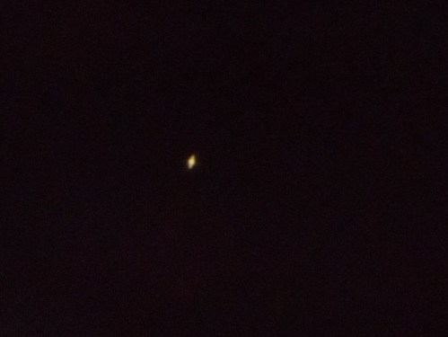 A small, bright object in a dark sky, possibly a star or planet, with a faint glow.