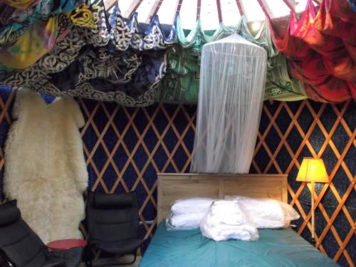 Cozy yurt interior with a bed, colorful draped fabric ceiling, and a soft chair, creating a warm, inviting atmosphere.