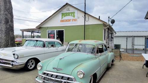 A vintage turquoise car parked outside Jerry's Smokin' Pig, a small restaurant with a green and white exterior.