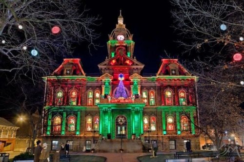 Historic building illuminated with festive red and green lights, featuring a Christmas tree, at night.