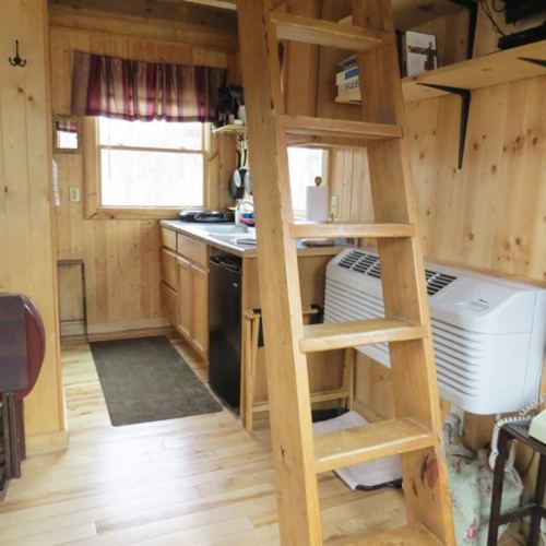 A wooden ladder leads to a loft in a cozy, rustic kitchen with wooden walls and appliances.