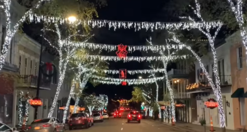 A festive street at night, adorned with white lights and decorations hanging from trees and buildings.