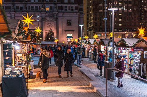 A festive market scene at night, with stalls, holiday decorations, and people browsing in a lively atmosphere.
