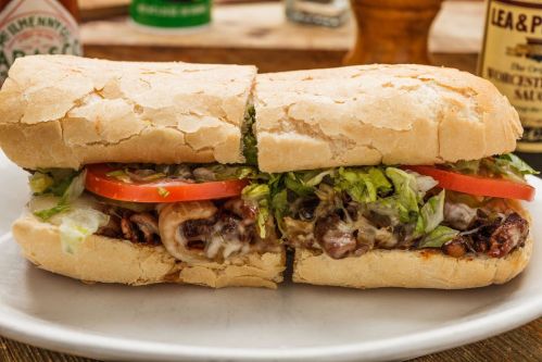 A close-up of a sandwich filled with lettuce, tomato, and a savory mixture, served on a crusty bread roll.