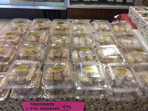 A display of packaged cucidati (fig cookies) in clear containers at a bakery, labeled with yellow stickers.