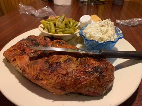 A plate featuring a large grilled steak, green beans, a side of potato salad, and a biscuit.