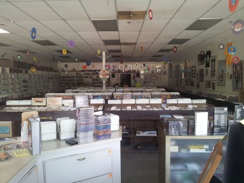 A spacious record store filled with shelves of vinyl records, CDs, and colorful decorations hanging from the ceiling.