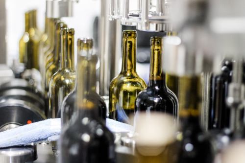 Bottles on a production line, with a blue cloth and machinery in the background, indicating a bottling process.