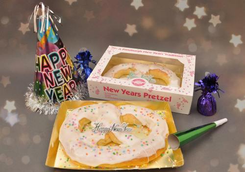A festive New Year's pretzel with icing and sprinkles, surrounded by party hats and decorations. Happy New Year!