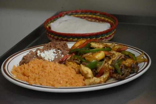 A plate of rice, refried beans, and sautéed vegetables with chicken, alongside a basket of tortillas.