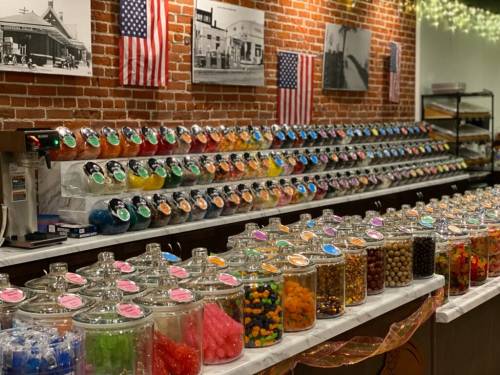 A colorful candy shop display with jars of sweets and a brick wall adorned with American flags and vintage photos.