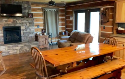 Cozy log cabin interior featuring a stone fireplace, wooden dining table, and comfortable seating area.