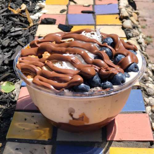 A delicious dessert bowl layered with yogurt, chocolate drizzle, blueberries, and coconut flakes on a colorful tiled surface.