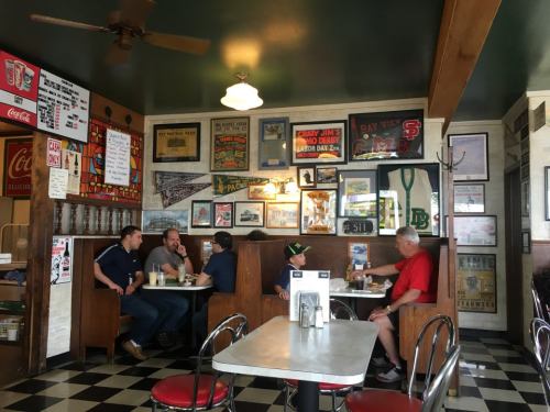 A cozy diner interior with patrons at booths, vintage decor, and a checkered floor.