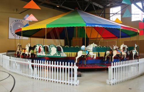 A colorful carousel with painted horses, surrounded by a white picket fence in a spacious indoor area.
