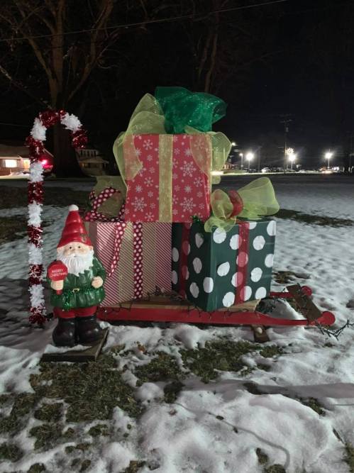 A festive display featuring a gnome, colorful wrapped gifts, and a sleigh on snow at night.