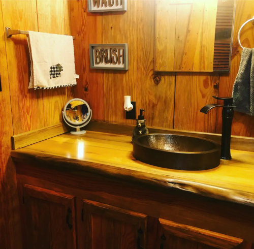 A rustic bathroom with wooden walls, a round sink, a black faucet, and decorative signs reading "WASH" and "BRUSH."