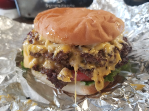 A juicy cheeseburger with melted cheese, lettuce, and tomato, served on a toasted bun and wrapped in foil.