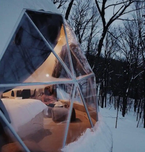 A cozy geodesic dome in a snowy forest, featuring a warm interior and large windows showcasing the winter landscape.