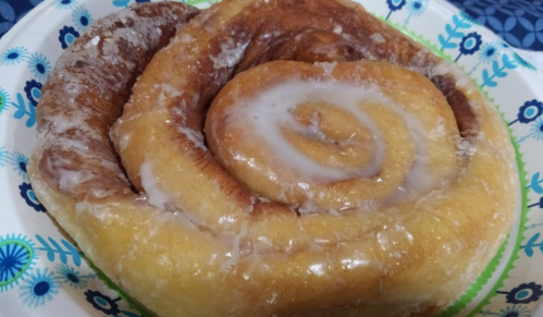 A close-up of a glazed cinnamon roll on a decorative paper plate.