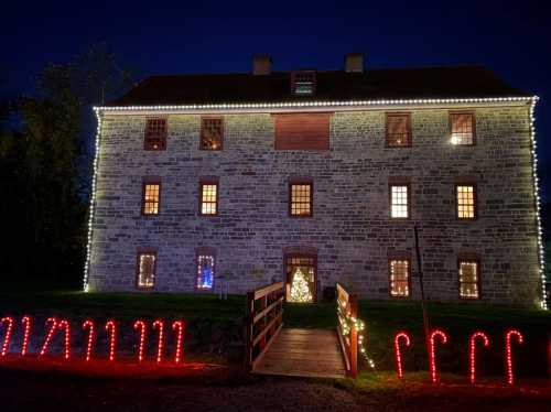 A stone building decorated with festive lights and candy canes, illuminated at night with a Christmas tree visible inside.