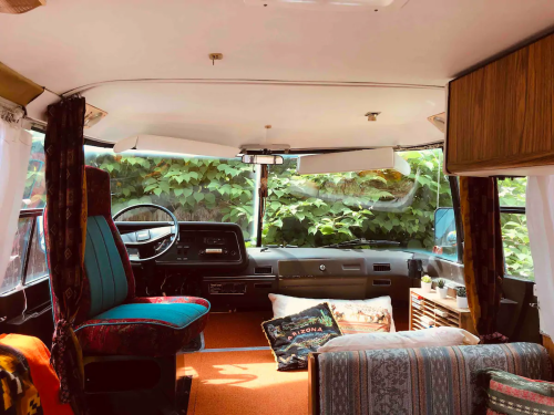 Cozy interior of a vintage camper van with colorful seating and plants visible through the windows.