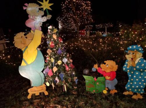 Berenstain Bears decorating a Christmas tree with colorful lights and ornaments in a festive outdoor setting.
