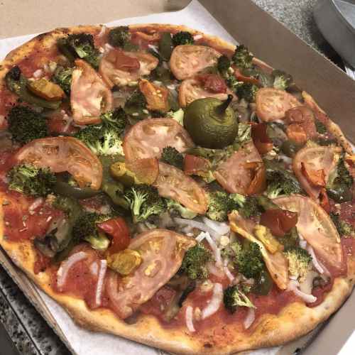 A freshly baked pizza topped with tomatoes, broccoli, green peppers, and olives in a pizza box.