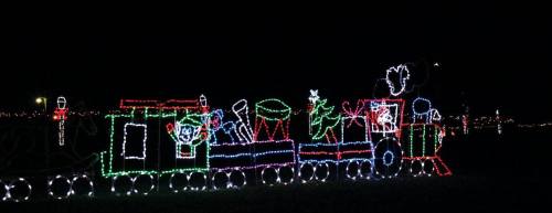 A colorful light display of a train decorated for the holidays, set against a dark night sky.