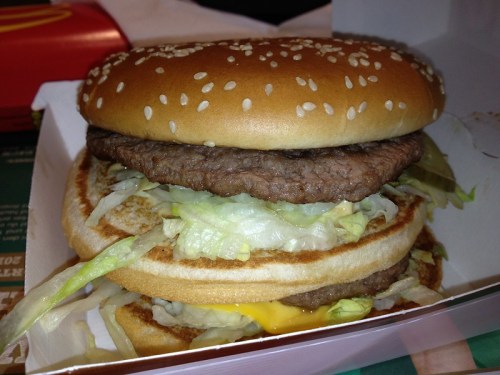 A close-up of a large hamburger with sesame seed bun, lettuce, and two beef patties with cheese.