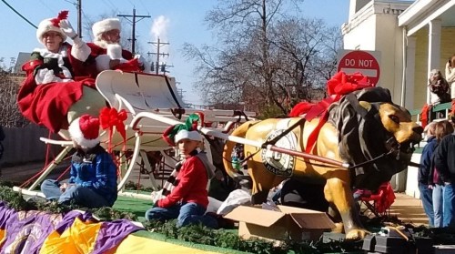Santa and Mrs. Claus on a festive float with a golden lion, surrounded by children and holiday decorations.