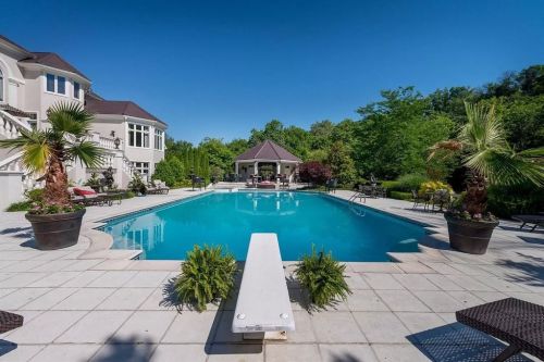 A luxurious pool surrounded by palm trees and lounge chairs, with a gazebo in the background and clear blue skies.
