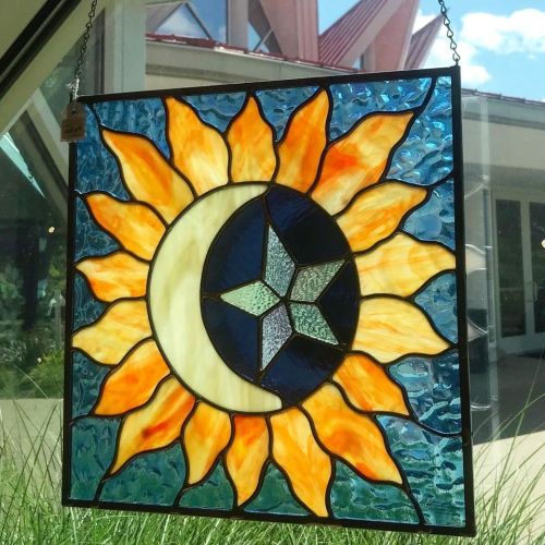 Stained glass window featuring a sun, moon, and star design in vibrant colors, hanging in natural light.