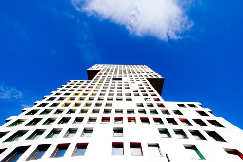 A modern, white building with colorful window frames, viewed from below against a bright blue sky.