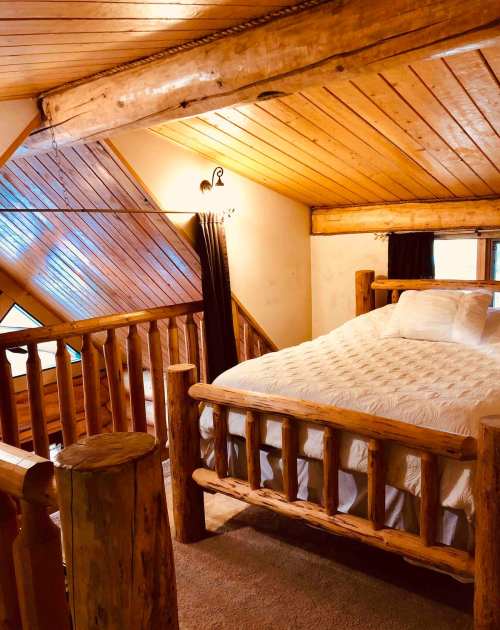 Cozy loft bedroom with a wooden bed, log accents, and sloped ceiling, featuring warm lighting and soft bedding.