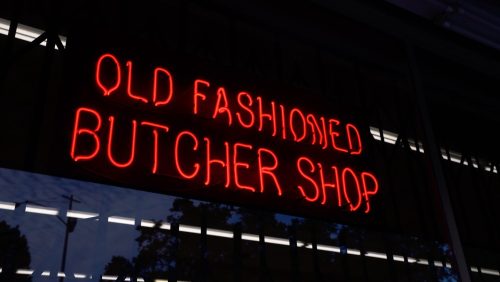Neon sign reading "Old Fashioned Butcher Shop" in bright red against a dark background.