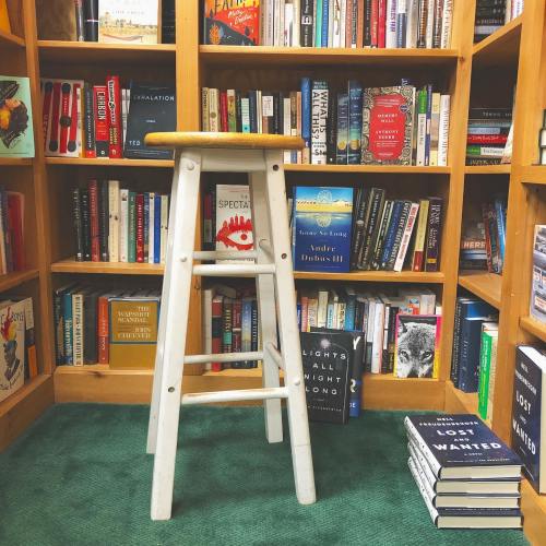A wooden stool in a cozy bookstore surrounded by shelves filled with various books.