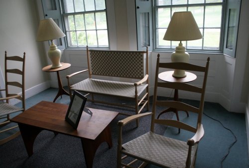 A cozy room with two chairs, a bench, a wooden coffee table, and lamps, featuring large windows with a view outside.