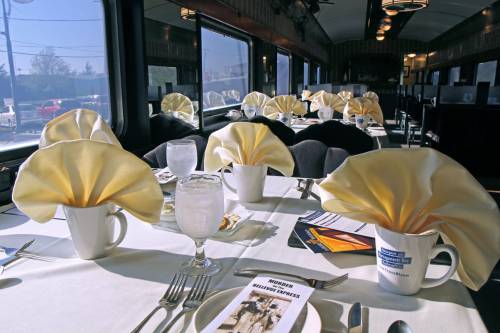 Elegant dining setup in a train car, featuring white tablecloths, folded yellow napkins, and glassware.