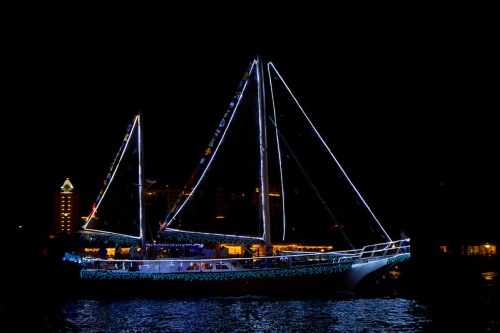 A brightly lit sailboat adorned with colorful lights glides through the water at night.