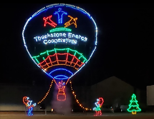 Colorful illuminated hot air balloon display with "Touchstone Energy Cooperatives" and festive decorations at night.