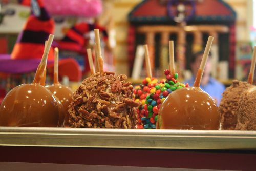 A display of caramel apples topped with nuts, candy, and chocolate, set against a colorful background.