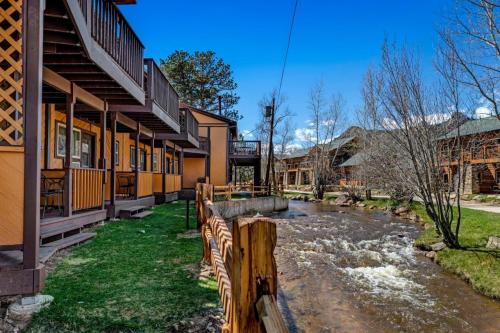 A scenic view of rustic buildings along a river, with trees and blue skies in the background.