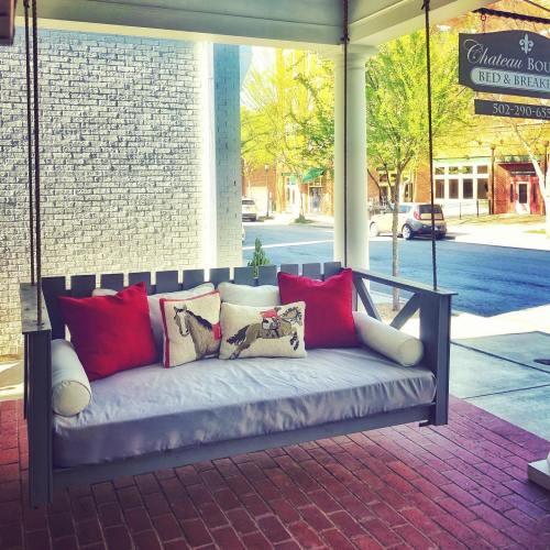 A cozy porch swing with red pillows, set against a brick floor and a view of a tree-lined street.