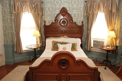 A cozy bedroom featuring a wooden bed, decorative pillows, and elegant curtains by two windows with lamps on side tables.